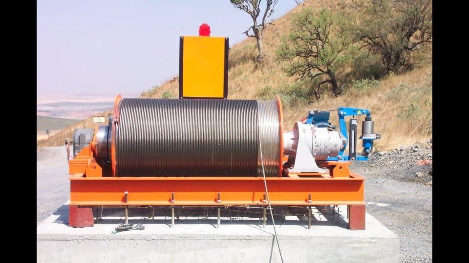 Winches SA custom electric shaft winder installed on a concrete foundation on site, with grooved steel wire-rope drum, gearbox drive and hydraulic brake unit, manufactured in Silverton, Pretoria for the Ingula Pumped Storage Scheme