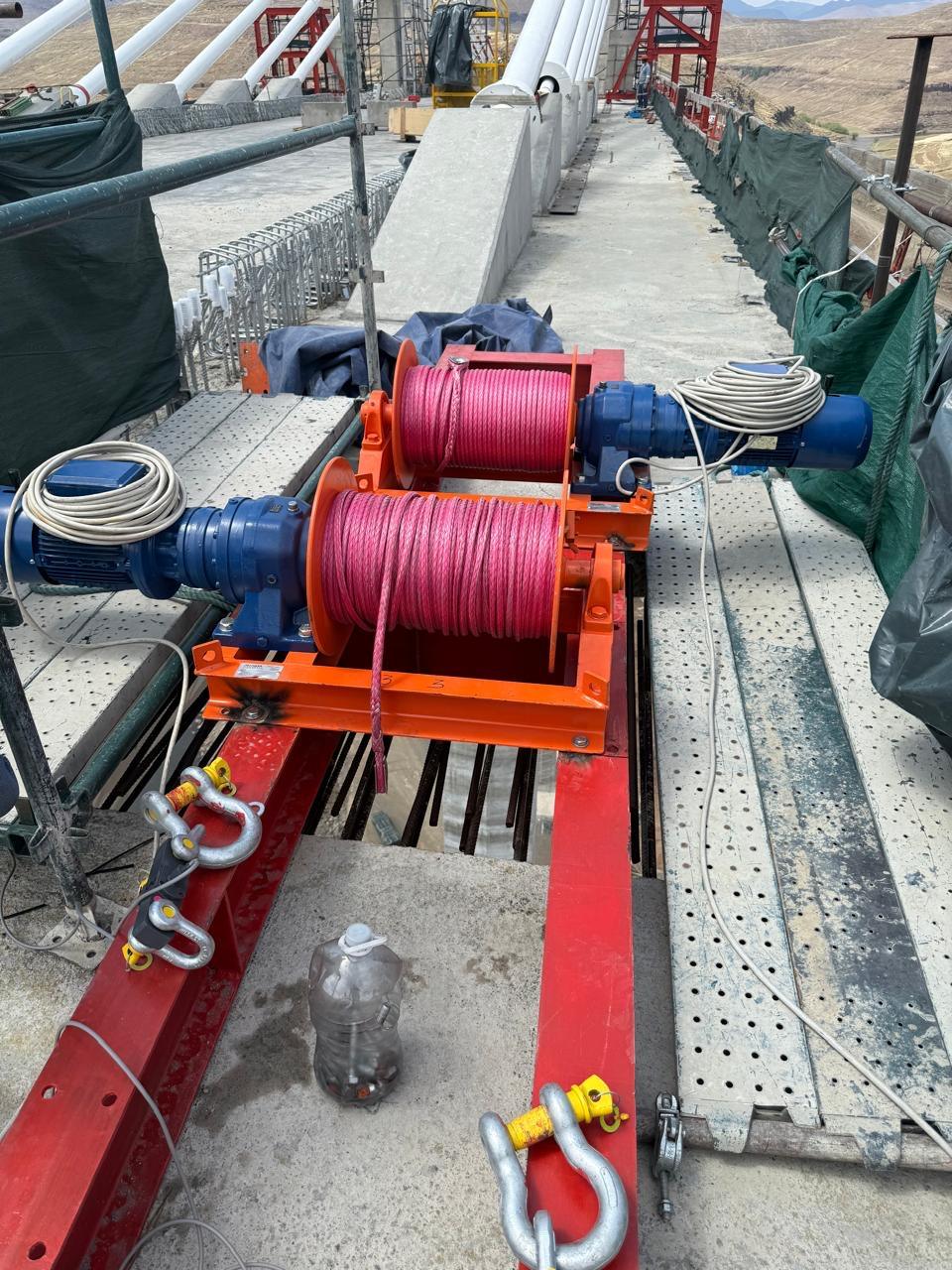 Two Winches SA electric winches with orange frames and synthetic rope drums mounted on the Senqu Bridge deck during construction, used for deck-level lifting work on the Lesotho Highlands Water Project Phase II